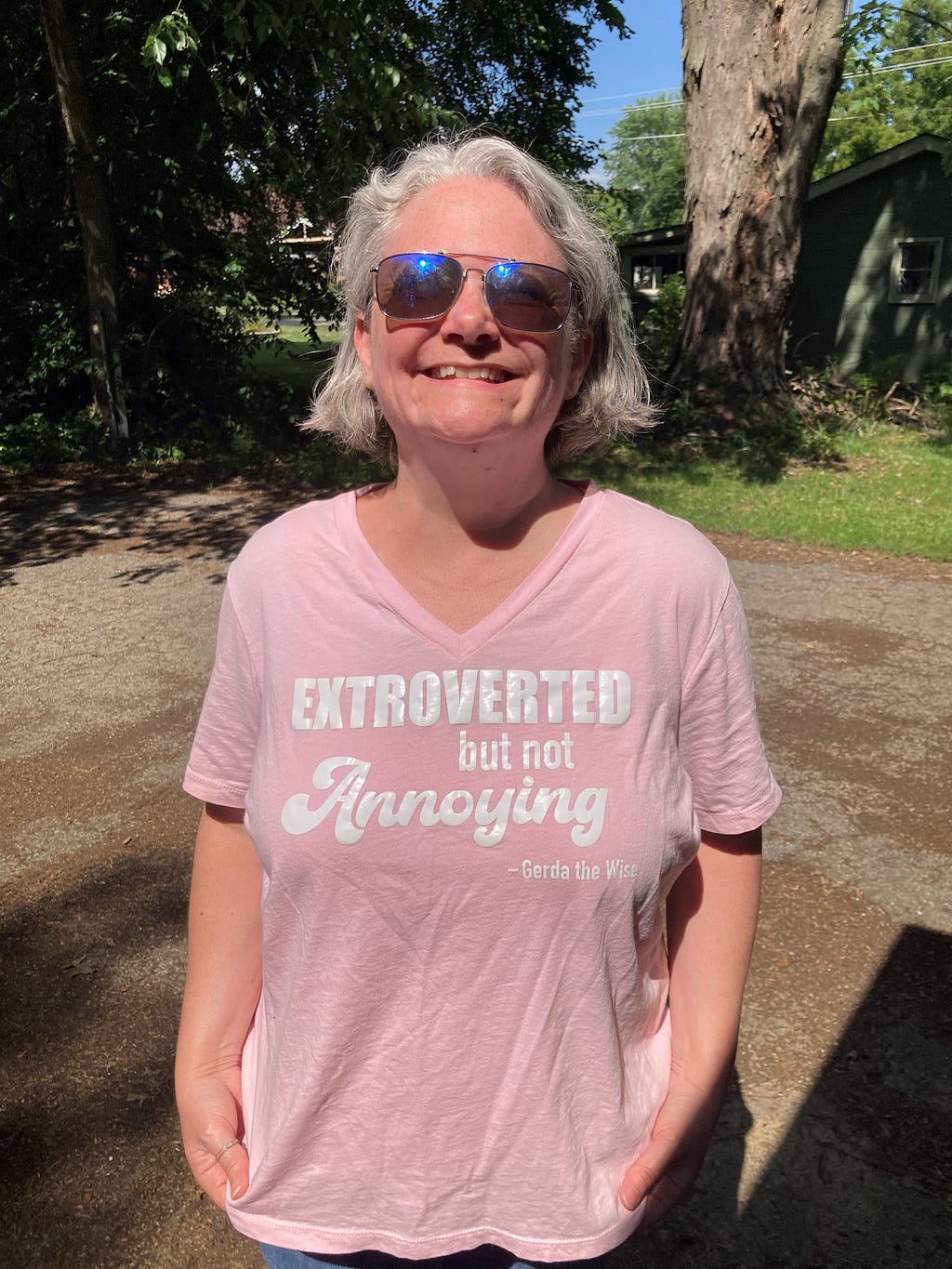 Picture of the author wearing blue sunglasses and a pink shirt that reads ‘Extroverted but not annoying.’