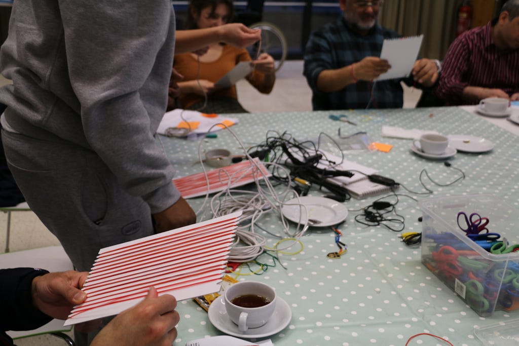 People sat around a table weaving wires around card.