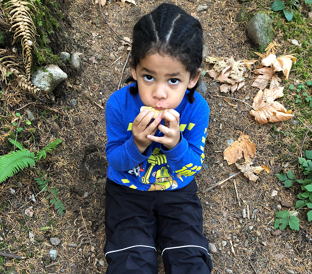 Child eating a snack sitting on the ground in the forest