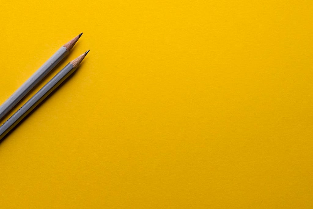 Two grey pencils atop a deep yellow background