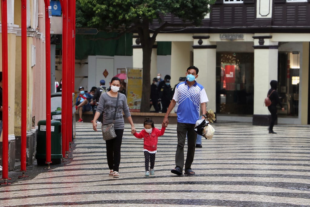 A couple and their child walk down the street, wearing masks and holding hands