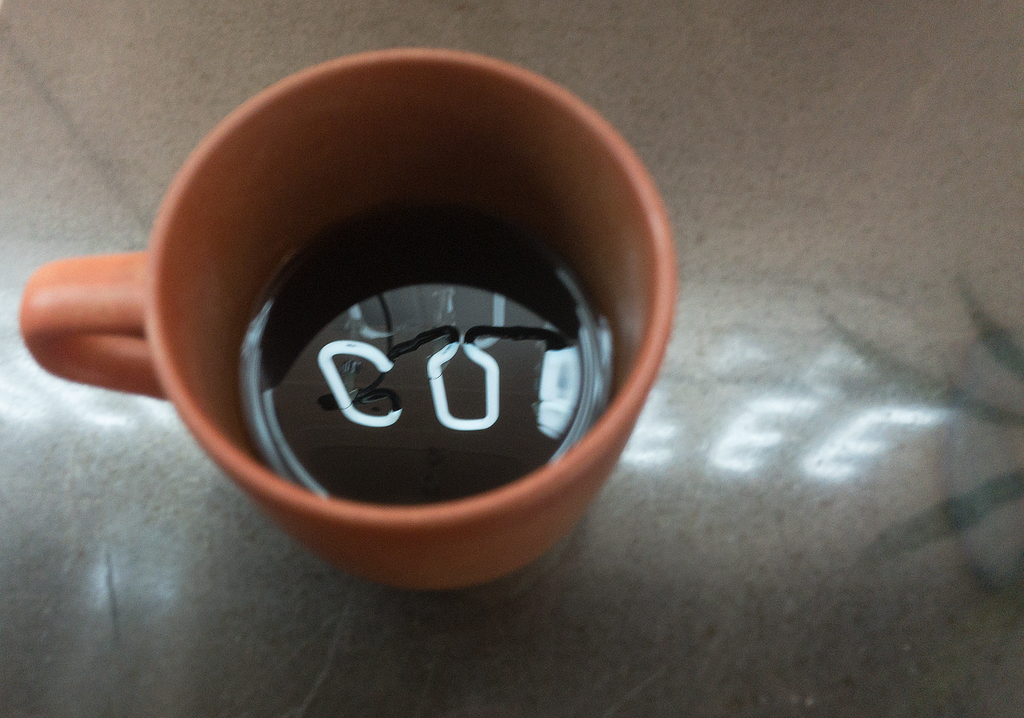 Coffee cup with a neon sign reflection of the work “COFFEE”