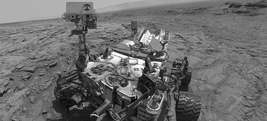 Selfie on Mars by NASA’s Curiosity rover, showing the rover on a flat crumbly Martian landscape.