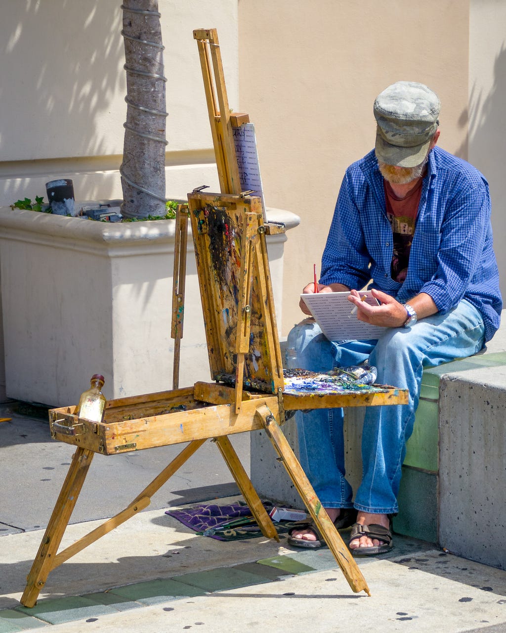A painter is seated at a portable easel in a city courtyard.