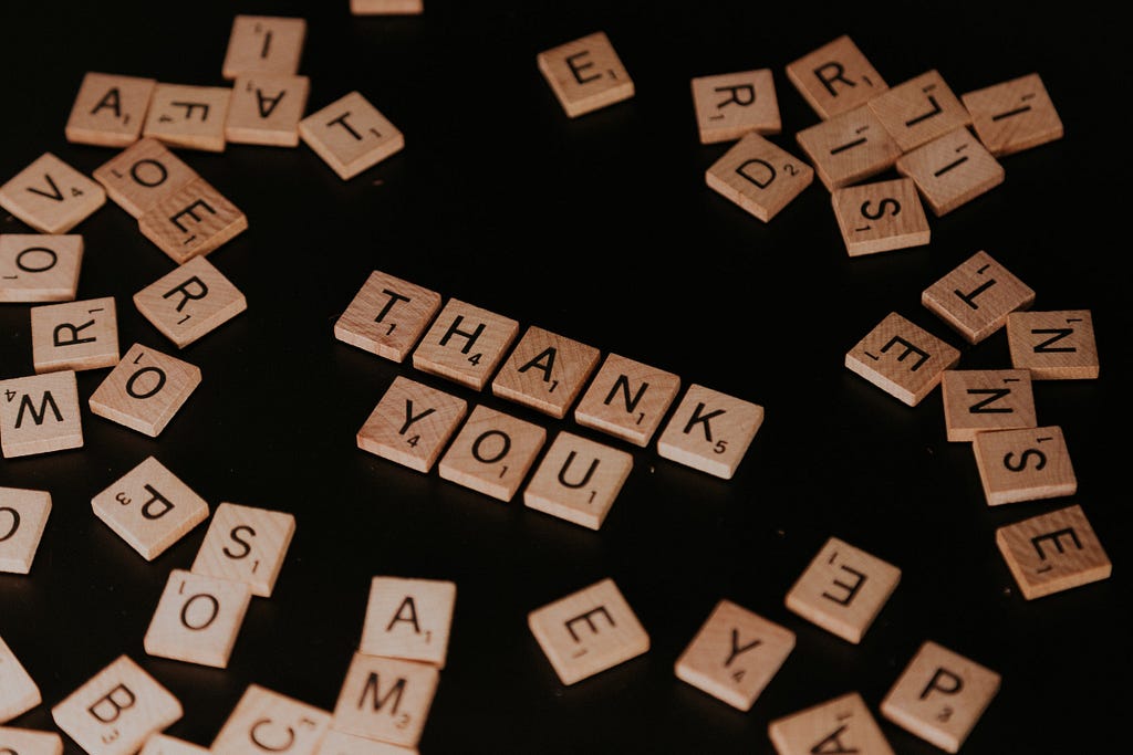 Scrabble characters are laid out against a black backdrop, with the words “THANK YOU” arranged in the center