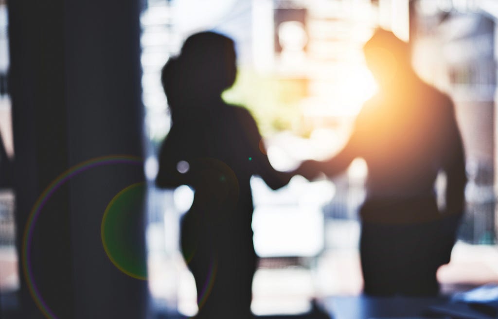 A photo of two businesspeople’s silhouettes as they shake hands.