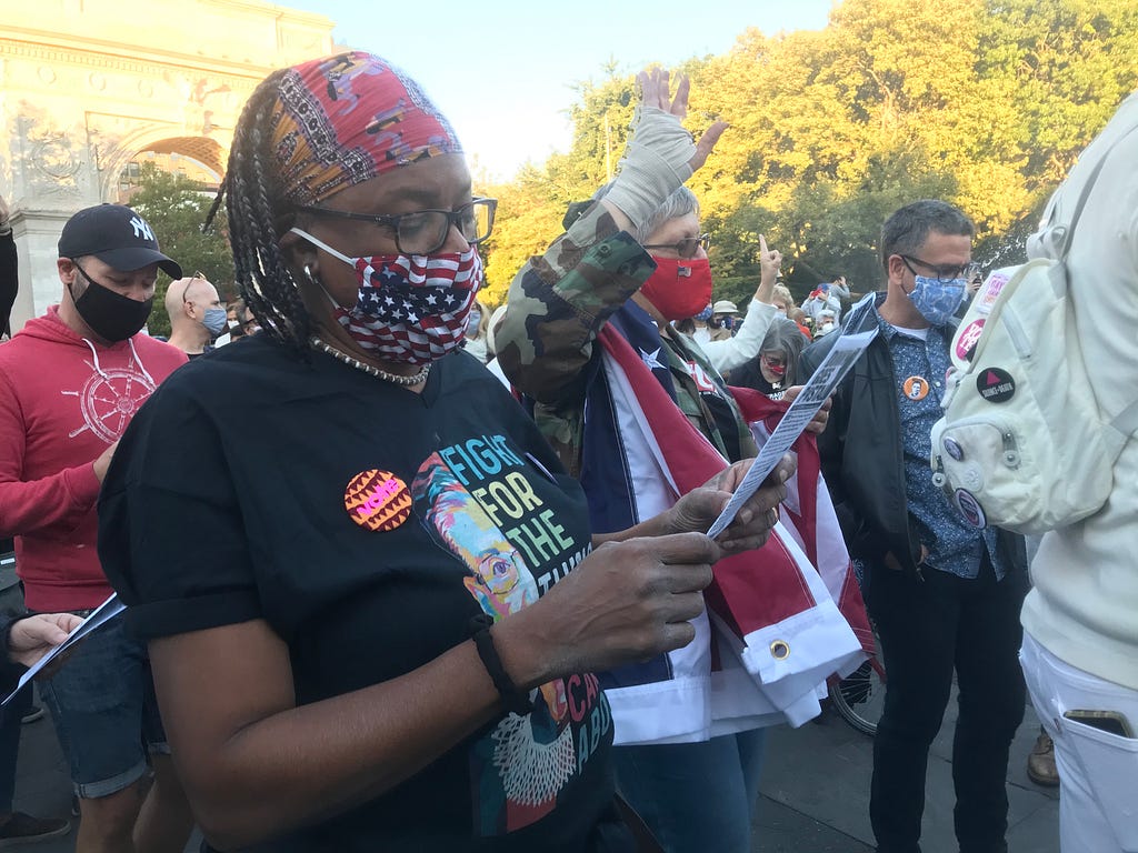 Cathy Marino-Thomas, with an American flag around her shoulders, holds up a hand while singing next to her wife.