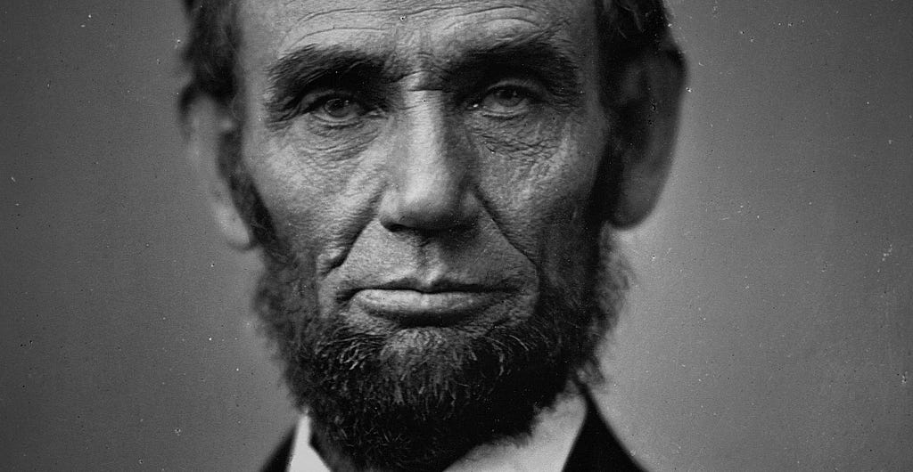 A close-up, black-and-white photo of Abraham Lincoln looking directly into the camera