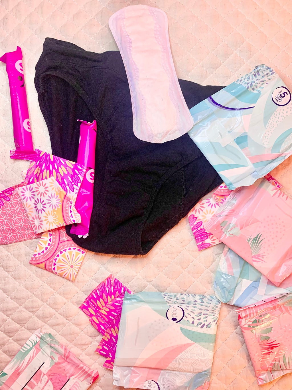 A variety of blue and pink floral print pads, tampons and dark coloured period panties randomly sprawled out across a white background