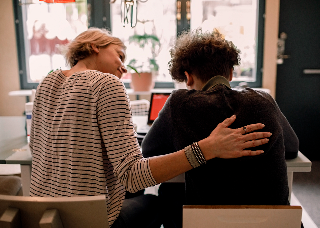 A woman with her hand assuringly on a younger person’s back.