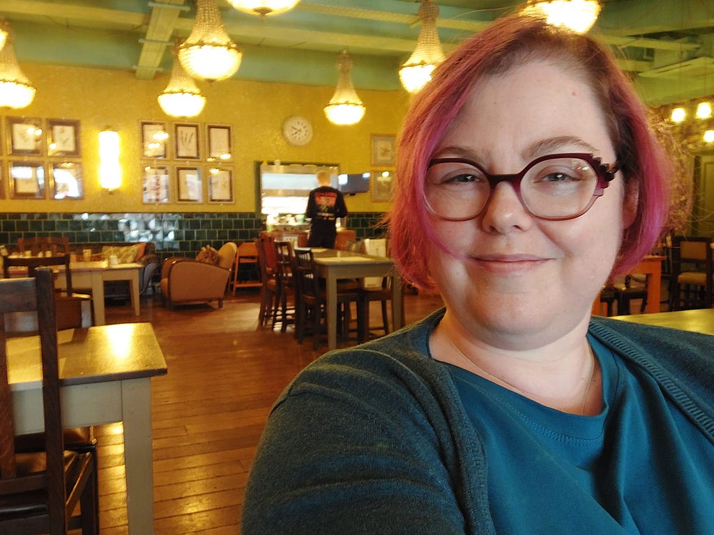 A selfie of Claire in a cafe, with tables and lights in the background