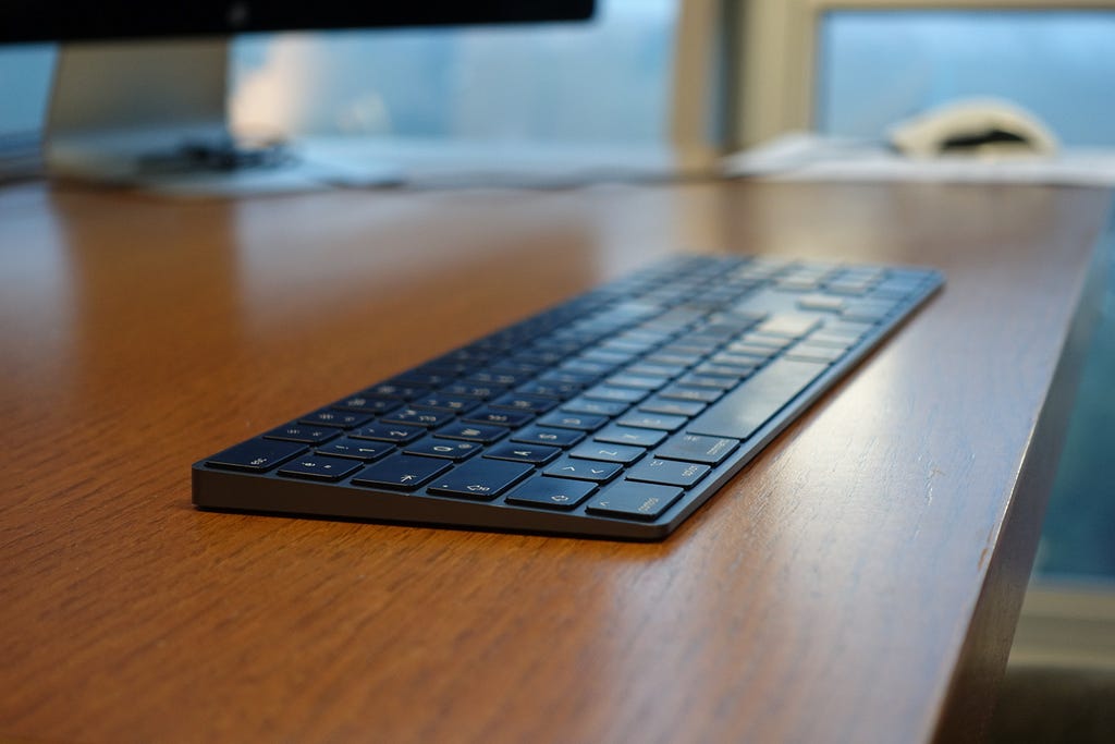 A close-up photo of a black iMac keyboard on a wooden table.