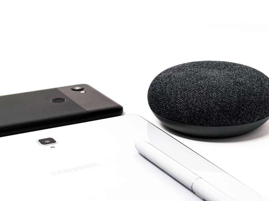 A smartphone, a Samsung tablet, and a Google home splayed out on a table.