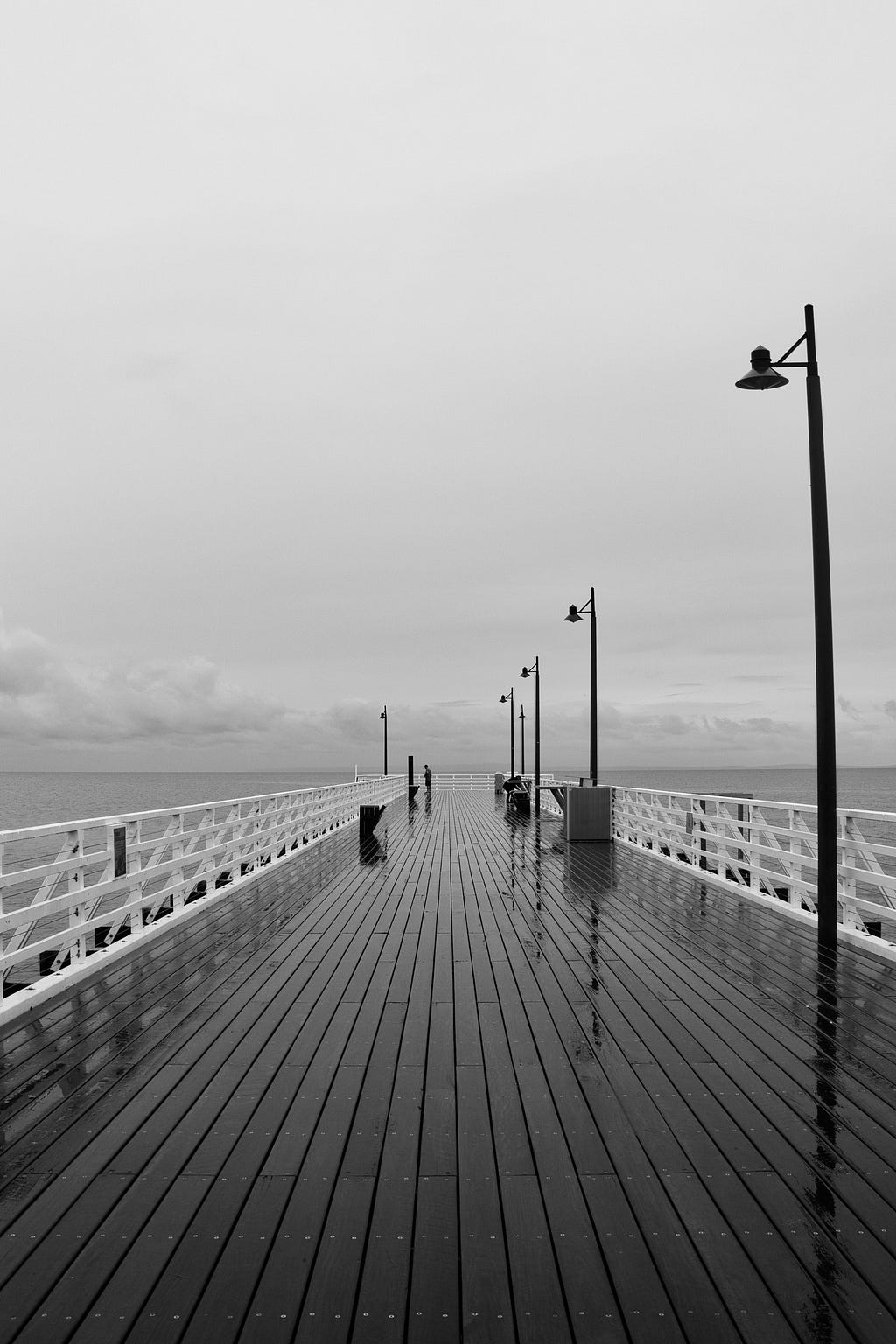 Black and white image of a wooden wet pier during a cloudy day