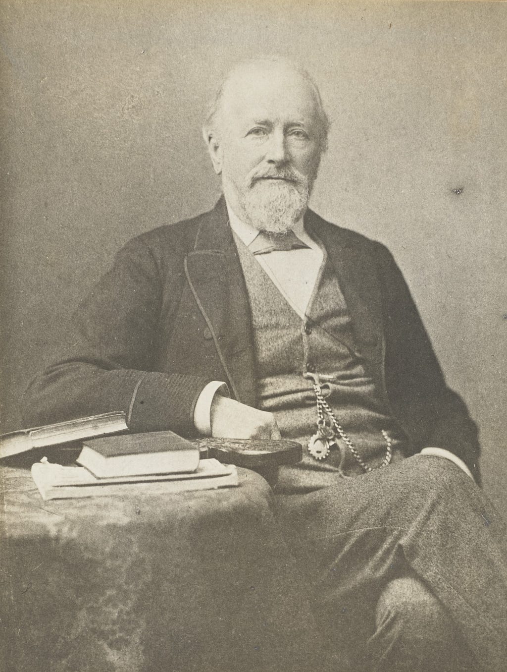 Black-and-white photograph of Edward Frankland, seated, leaning on a table with a stack of books.