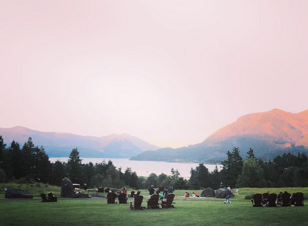 chairs on a grass hill overlooking river and surrounding hills in a pink dusk.