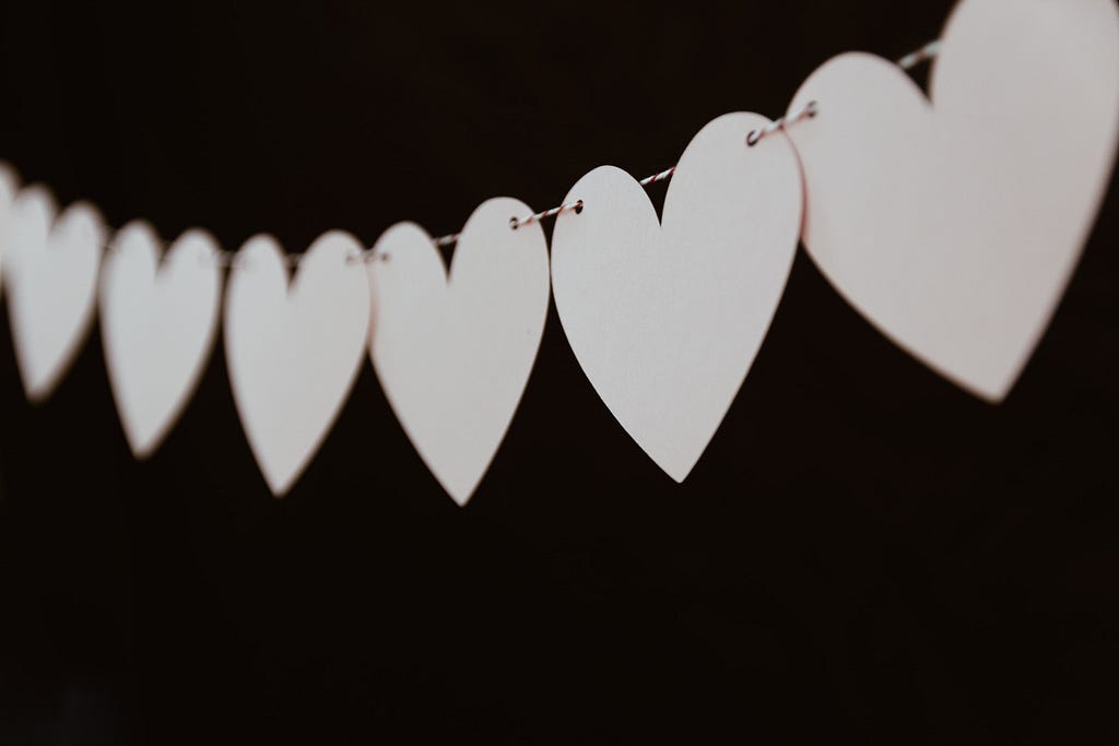 A string of white paper hearts stands out against a black background.
