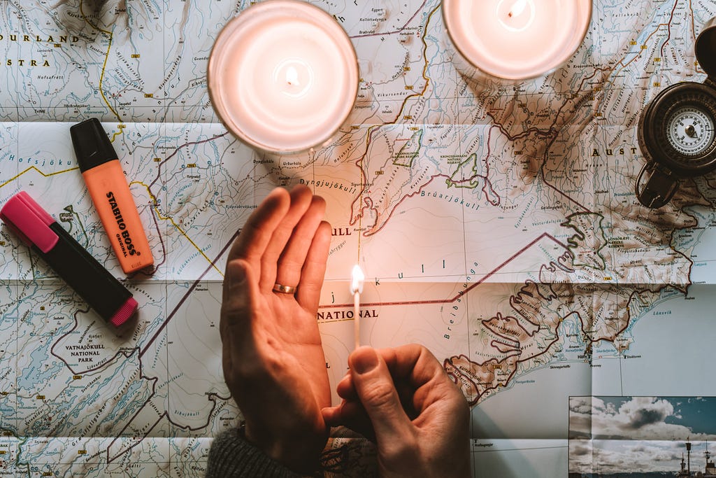 A map with some highlighter pens on it, some candles and a compass.