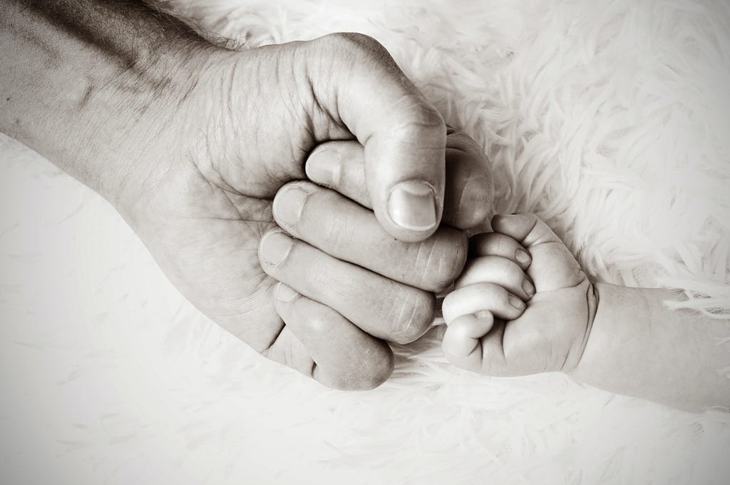 black and white photo of adult hand against baby hand, gentle fist-bump