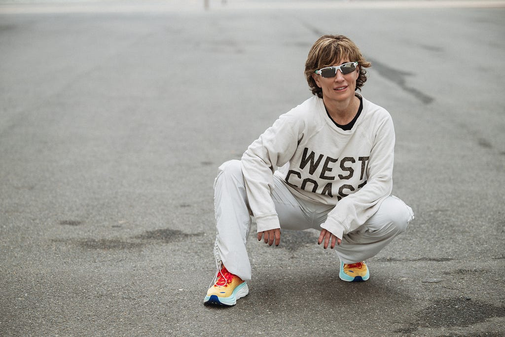 A picture of the author with cool white sunglasses in an athletic crouched position in sneakers and a “West Coast” off white sweatshirt.