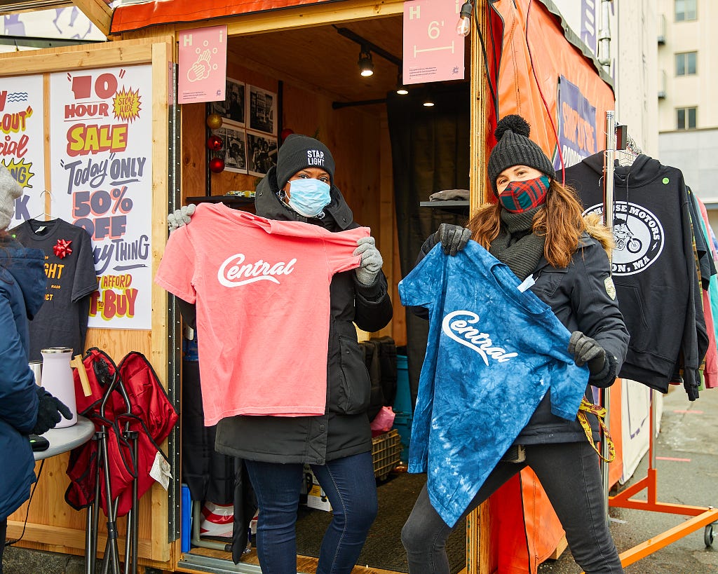 Holiday shoppers hold t-shirts and pose for the camera at a Winter Places market in Cambridge, MA.