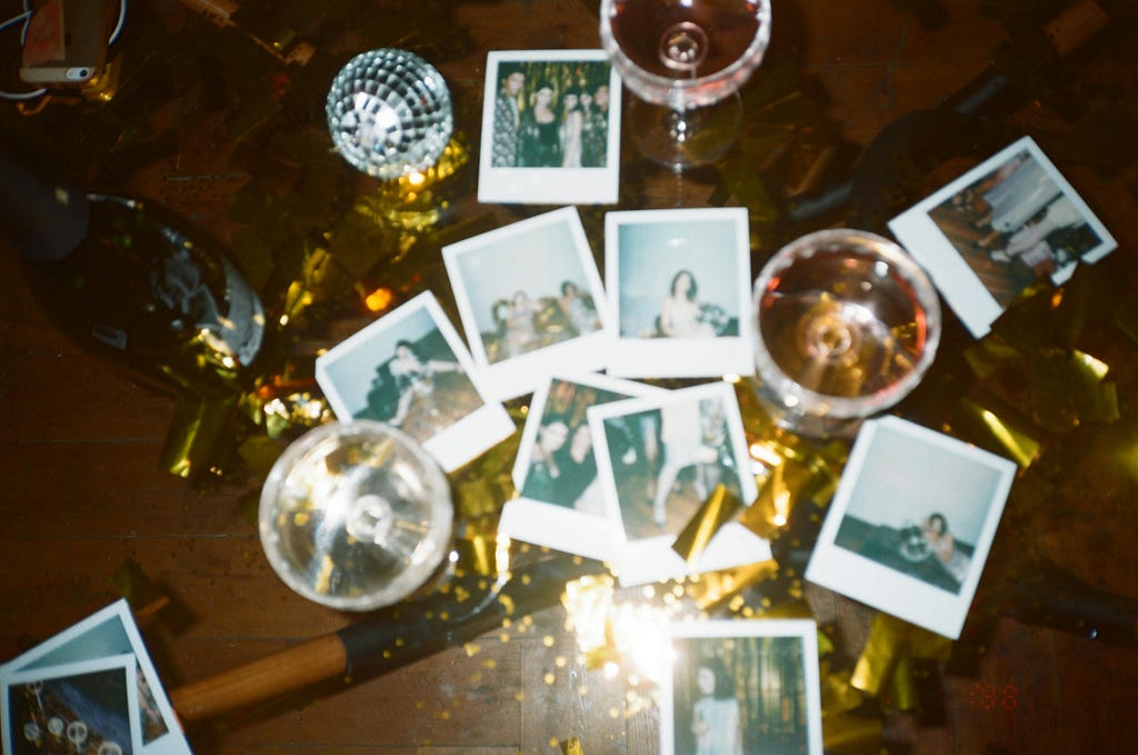 An after party mess of wine glasses, golden confetti and polaroid pictures on a glass-top table