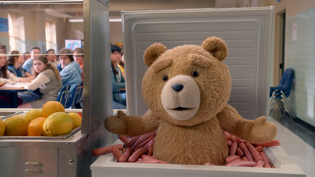 Ted has just scared a lunch lady to death by popping out of the box full of wieners exclaiming “I’m the King of the Wieners!” in the cafeteria, which sends him directly to the principal’s office. Credit: Peacock