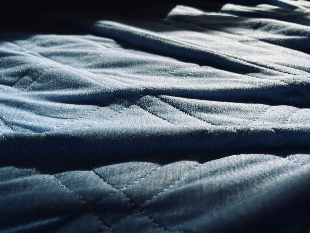 A wrinkled blue bed sheet with vividly contrasted shadows between each wrinkle.