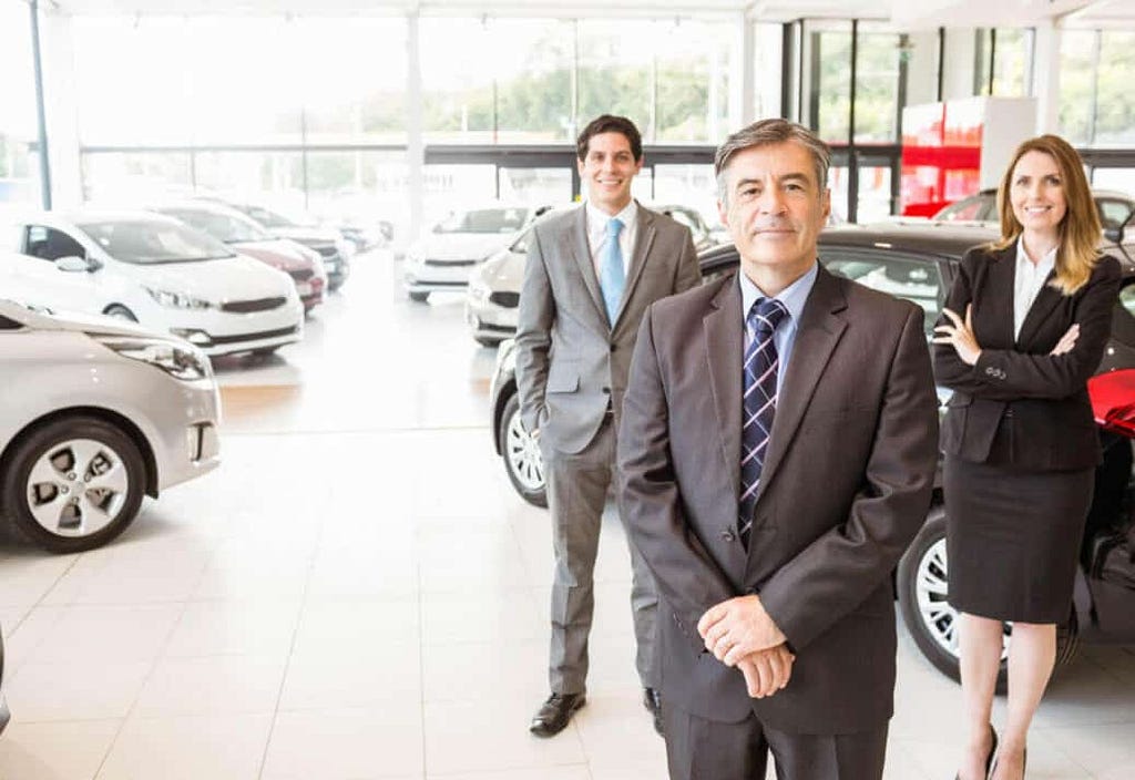 3 dealers standing inside a showroom looking at the camera.