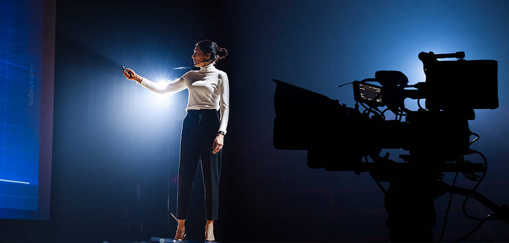 A woman gives a presentation in front of a digital cinema camera.