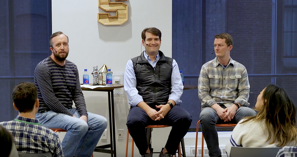 Three men sitting in stools on a stage.