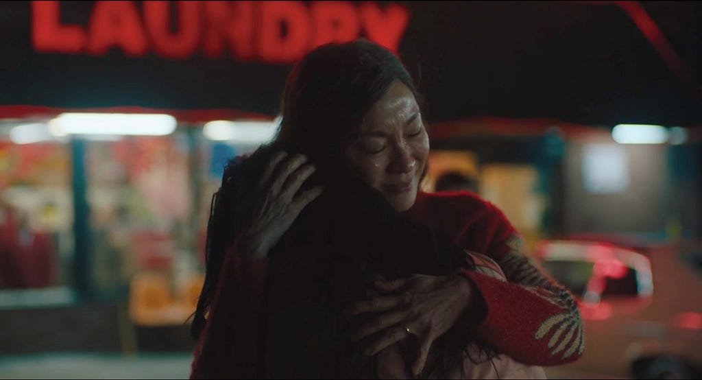 A mother (Evelyn Wang) embraces her daughter (Joy Wang) outside of a laundromat with red neon lights