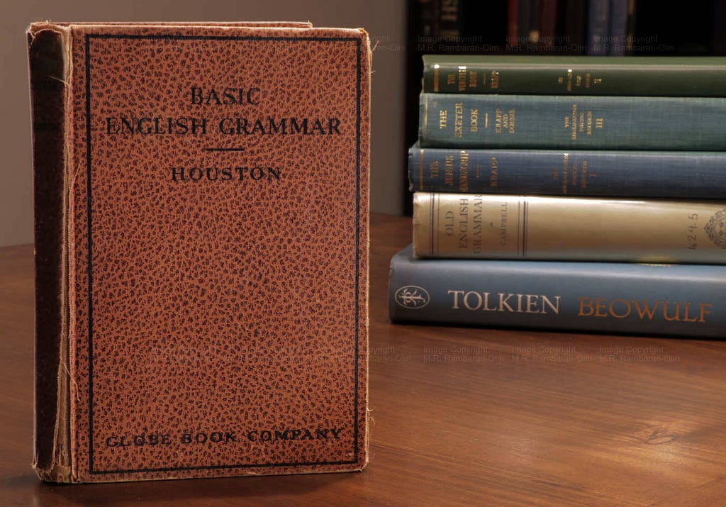 An upright copy of the book, “Basic English Grammar” next to a stack of books.