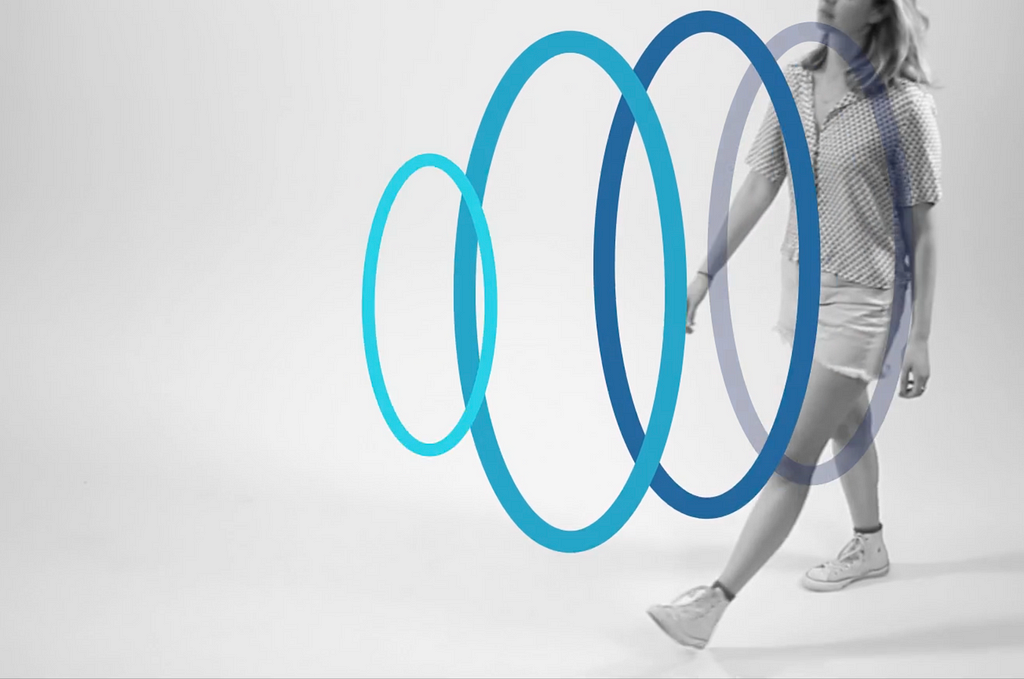 The image shows a person walking in a minimalist space with overlapping blue rings superimposed over their body. The rings seem to represent the direction of walking with an invisible digital layer.