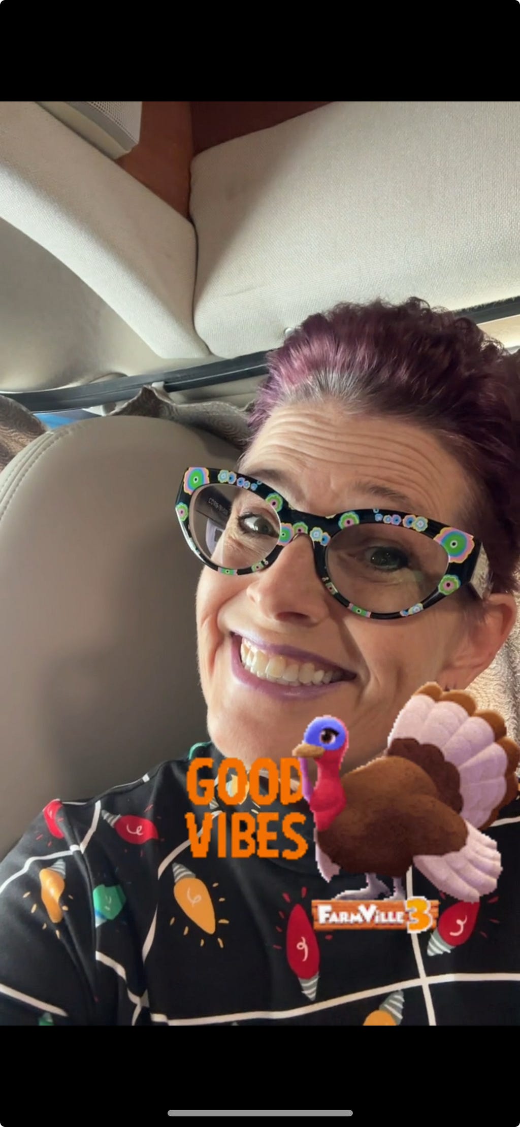 CC in a shirt with holiday lights printed on it. Her fun flowered glasses and a big smile with a Turkey sticker that says Good Vibes — This is a screenshot from the video. Scroll for video.