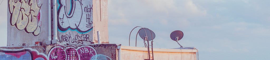 The top of a graffiti-covered building in Brooklyn with a partly cloudy sky behind it.