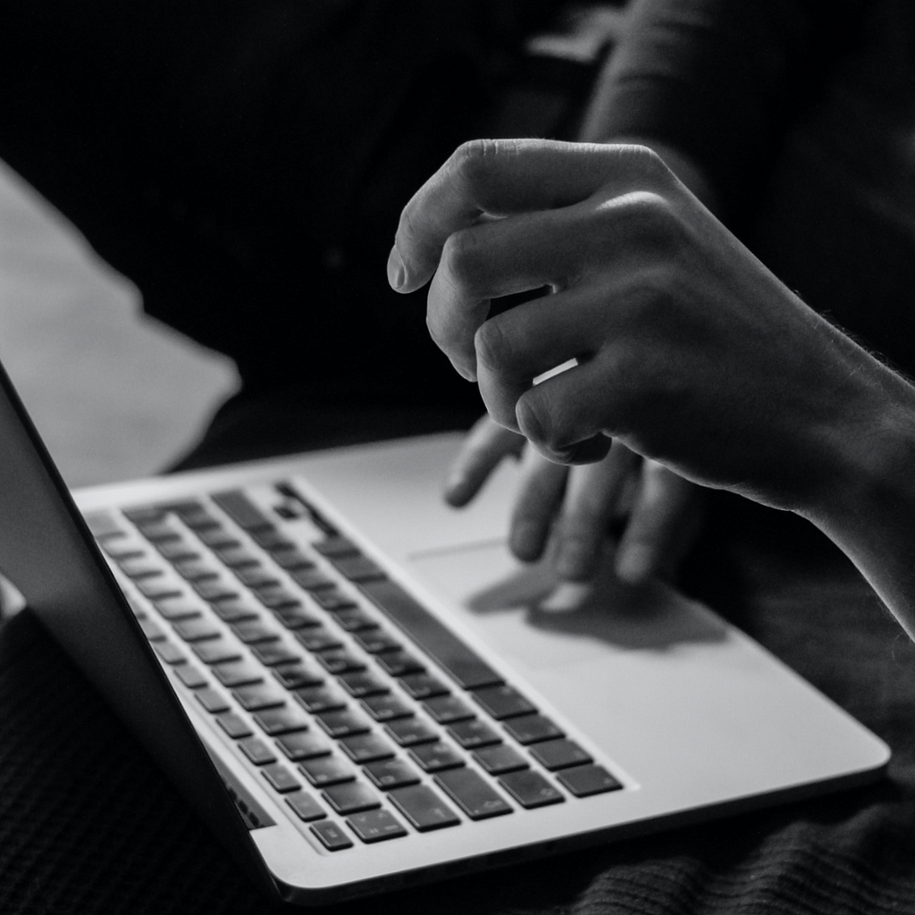 A black and white close up photo of hands using a laptop.