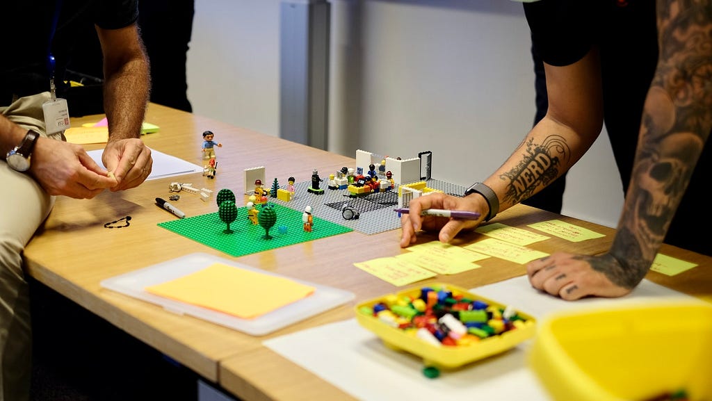 Pessoas construindo um protótipo de serviço, utilizando legos e anotando em post-its.