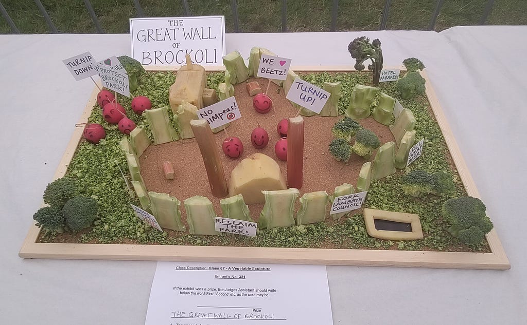 Sculpture of Brockwell Park — complete with wall and protest signs — made out of vegetables.