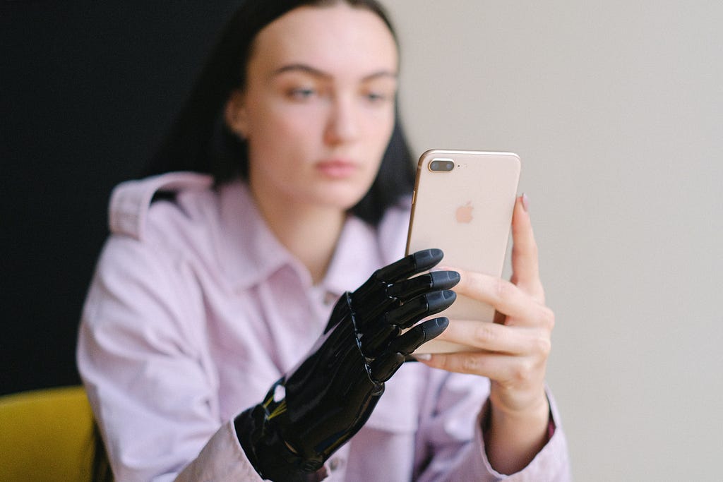 A young woman with a bionic right hand holds and looks at her phone.