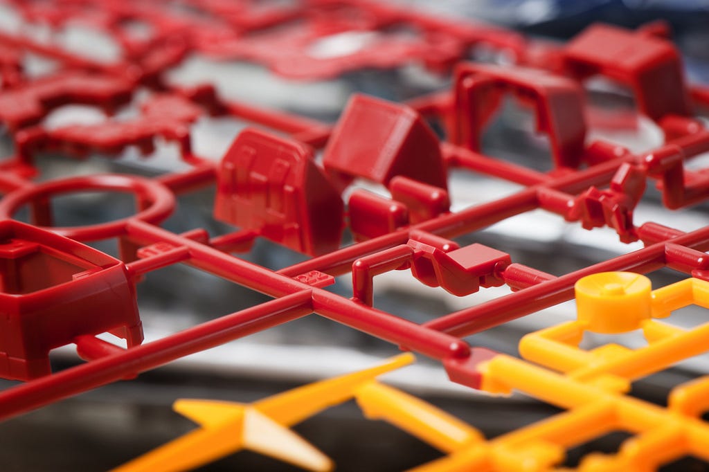 The components of a red toy are injected and molded at a rapid pace. Here they are, with plastic scrap from the injection process still attached. Small components like those found in consumer products are perfect for injection molding.