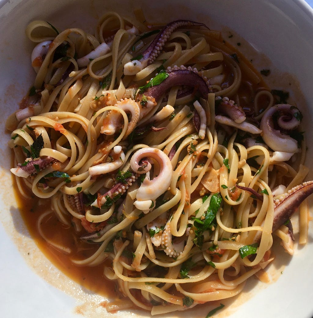 Closeup of a plate of linguini with small, curled squid tentacles.