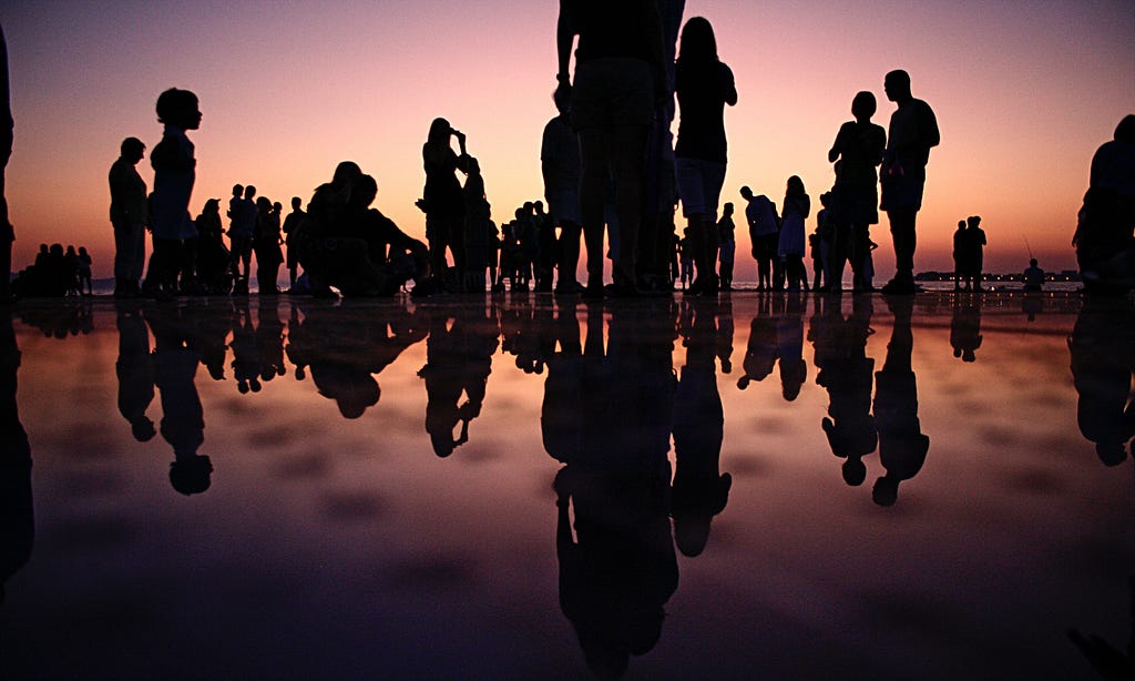 Silhouettes of people on a reflective ground against sunset.
