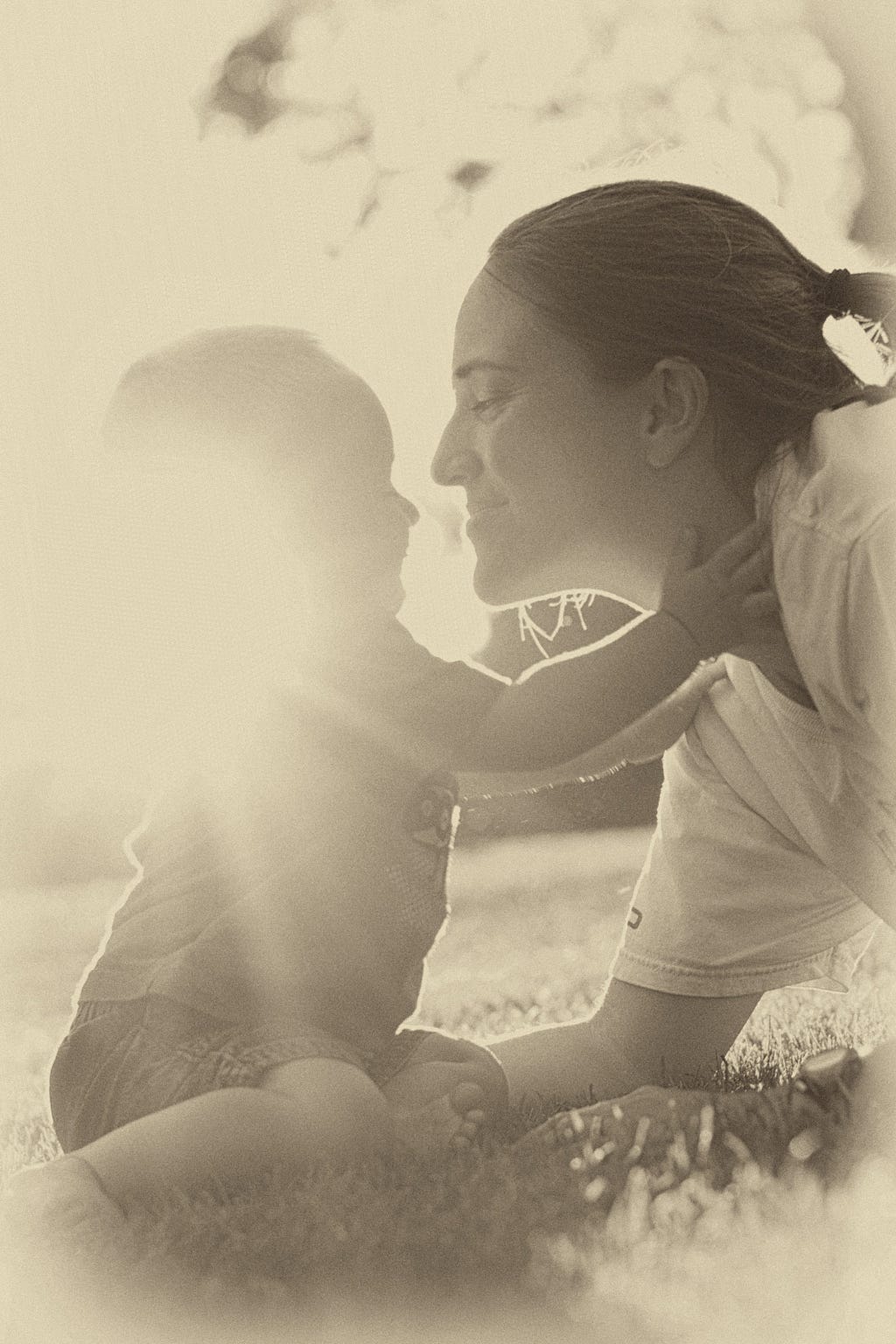 Baby reaching for Mom who is leaning down and smiling at him.