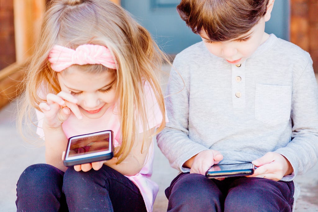 Photograph of two children playing on mobile devices