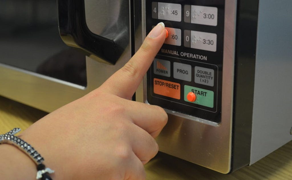Image of a person using a microwave with button engraved with braille.