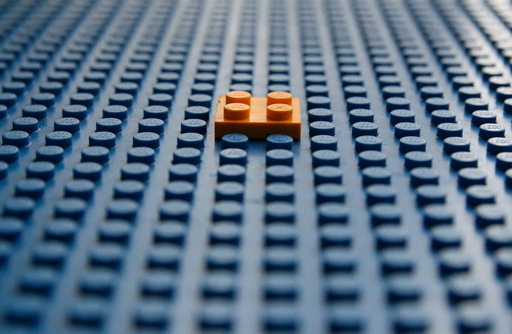 Placa de lego azul, com uma peça de lego laranja sobre ela.