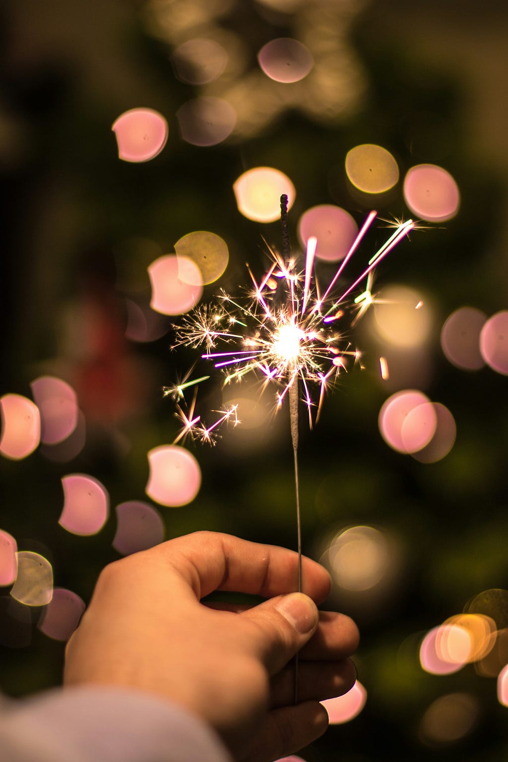 A hand holding out a single lit sparkler. Author used this image to connect to her celebration of one year on Medium.