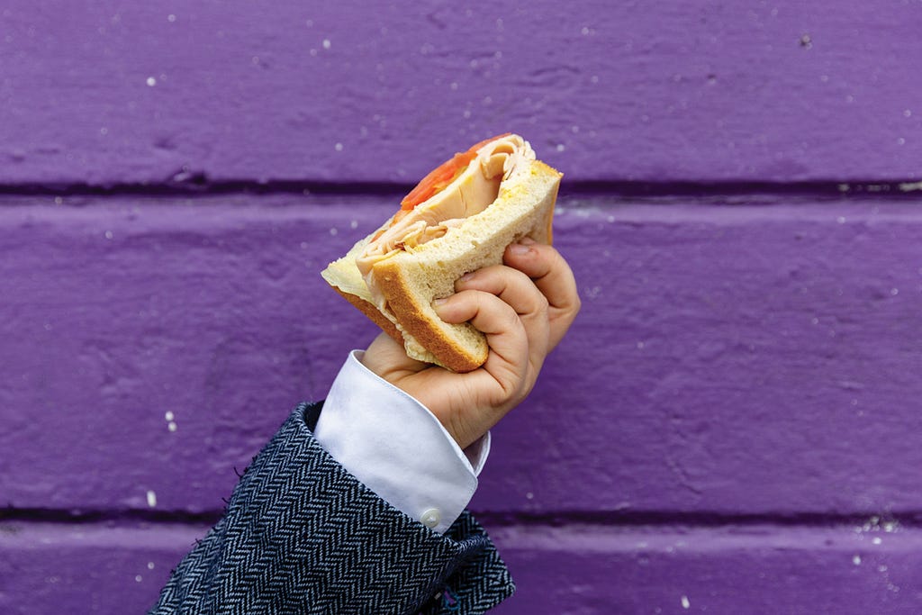 Carrie Bishop holding a tomato-cheese sandwich in front of a purple wall