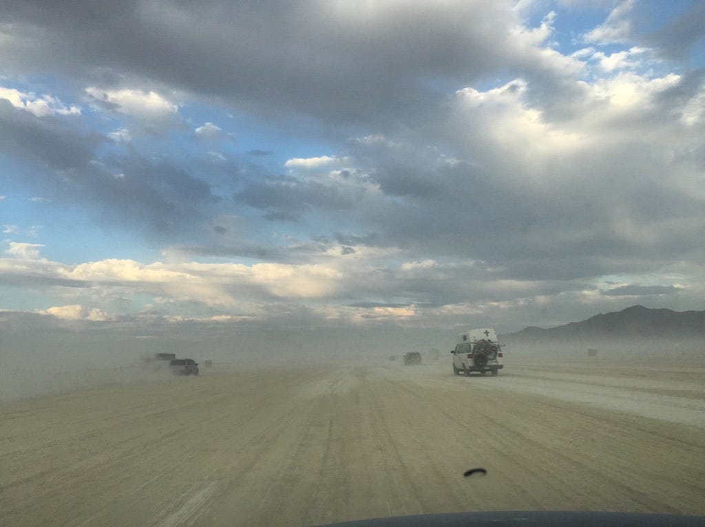 A picture of a dusty road with three visible vehicles.